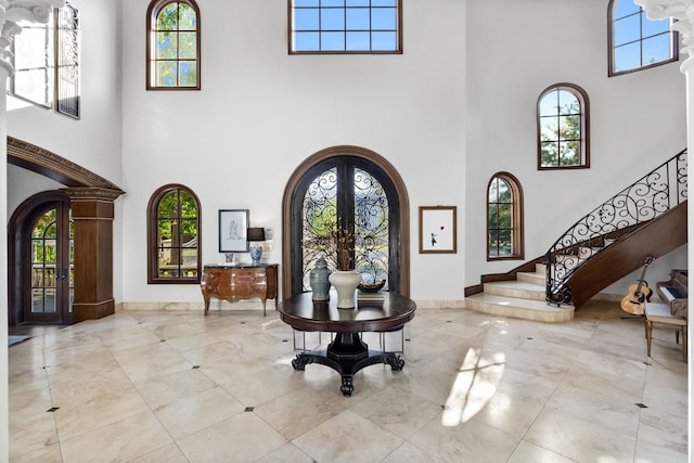 entryway featuring french doors, arched walkways, baseboards, a towering ceiling, and stairs
