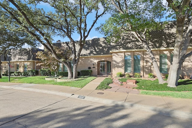 french country style house featuring brick siding, roof with shingles, and a front yard