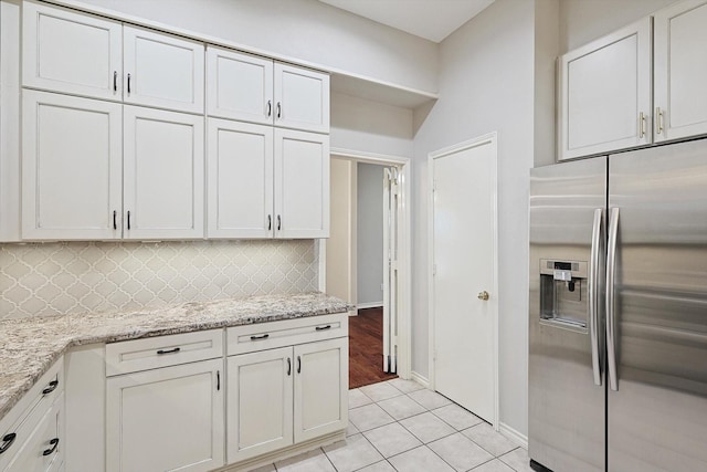 kitchen featuring light tile patterned floors, light stone countertops, baseboards, decorative backsplash, and stainless steel fridge