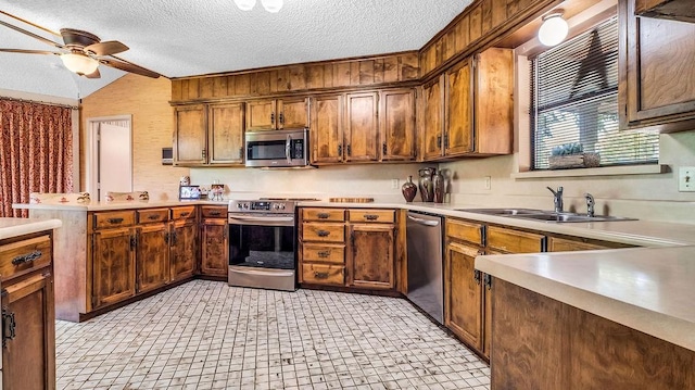kitchen with light countertops, a sink, a peninsula, appliances with stainless steel finishes, and ceiling fan