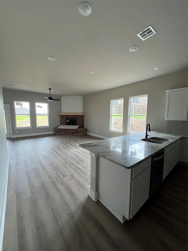 kitchen with dishwasher, visible vents, a ceiling fan, a sink, and a brick fireplace
