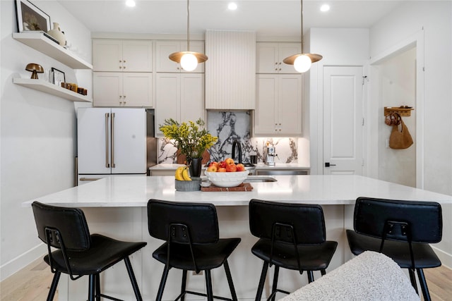 kitchen with hanging light fixtures, a kitchen island with sink, light wood-type flooring, freestanding refrigerator, and recessed lighting