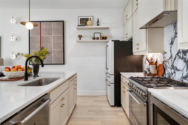 kitchen featuring light wood finished floors, under cabinet range hood, a sink, light stone countertops, and appliances with stainless steel finishes
