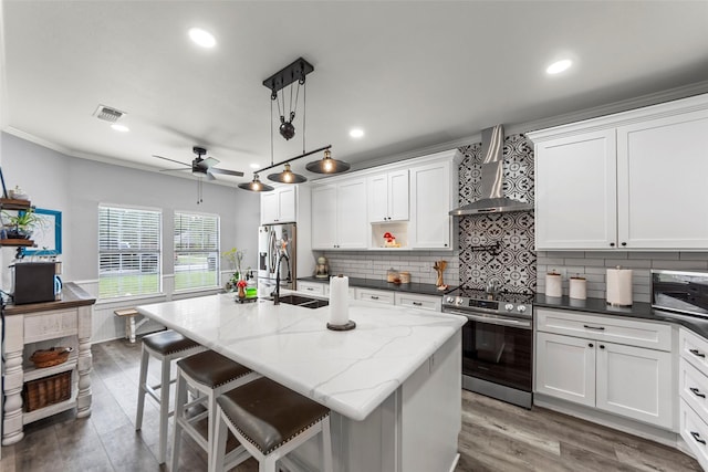 kitchen with wall chimney range hood, a sink, ceiling fan, stainless steel appliances, and white cabinets