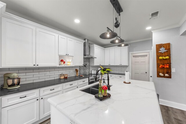 kitchen featuring wall chimney exhaust hood, baseboards, visible vents, backsplash, and ornamental molding