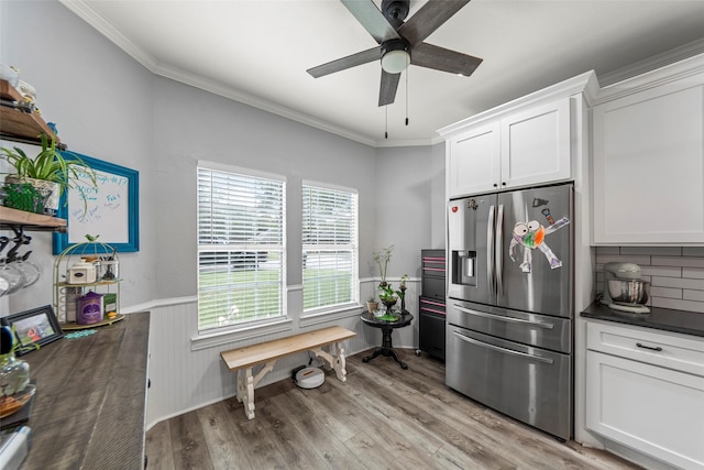 kitchen with dark countertops, white cabinetry, a ceiling fan, stainless steel refrigerator with ice dispenser, and ornamental molding