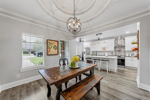 dining room featuring a raised ceiling, light wood-type flooring, baseboards, and ornamental molding