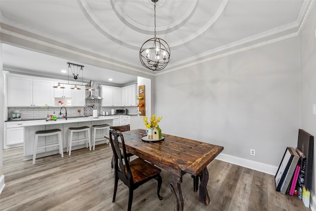 dining space featuring crown molding, light wood-style floors, a tray ceiling, baseboards, and a notable chandelier