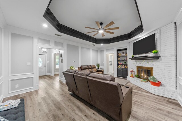 living room featuring a ceiling fan, light wood-style floors, a decorative wall, crown molding, and a brick fireplace