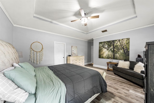 bedroom with a ceiling fan, wood finished floors, a tray ceiling, baseboards, and visible vents