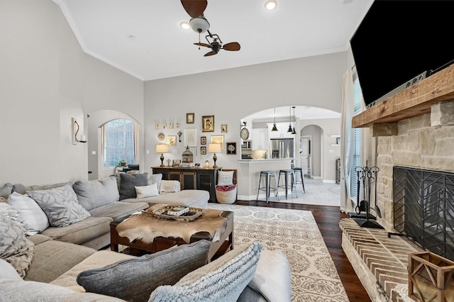 living area with arched walkways, crown molding, dark wood-style flooring, and a high ceiling