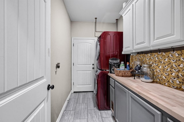 laundry area with cabinet space, wood tiled floor, baseboards, and stacked washer / dryer
