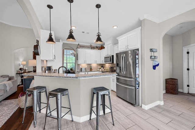 kitchen with light stone counters, a breakfast bar, arched walkways, a peninsula, and appliances with stainless steel finishes