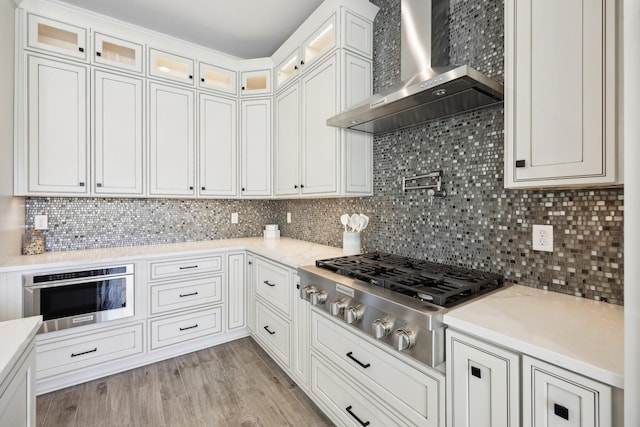 kitchen featuring glass insert cabinets, backsplash, appliances with stainless steel finishes, and wall chimney range hood