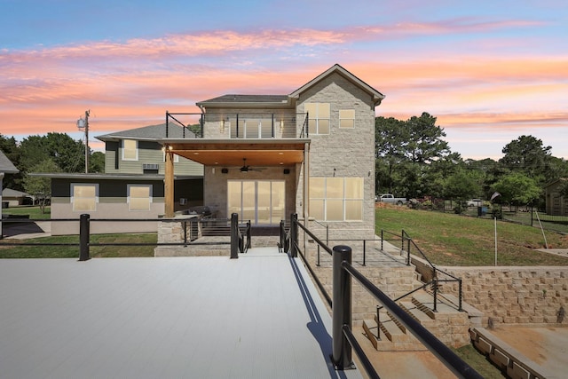 modern home featuring a front lawn, a balcony, ceiling fan, a patio, and stone siding