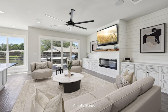 living room with recessed lighting, wooden walls, wood finished floors, a glass covered fireplace, and ceiling fan