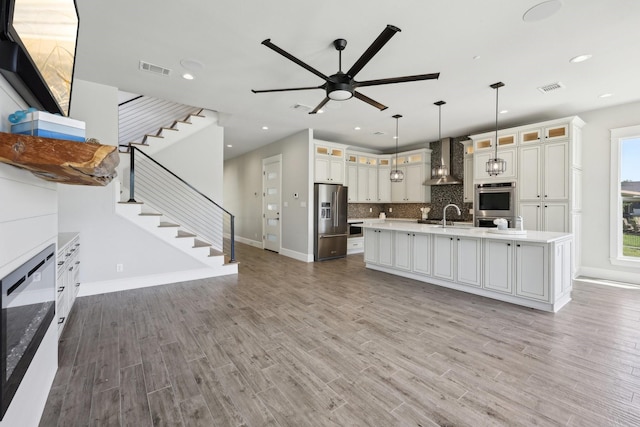 kitchen featuring a ceiling fan, light countertops, wall chimney exhaust hood, appliances with stainless steel finishes, and visible vents