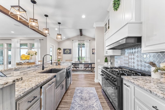 kitchen with vaulted ceiling, a sink, double oven range, decorative backsplash, and light wood-style flooring
