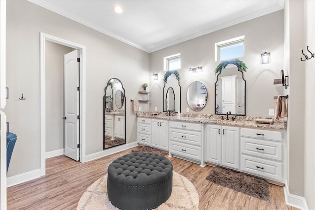 full bath with double vanity, wood finished floors, crown molding, and a sink