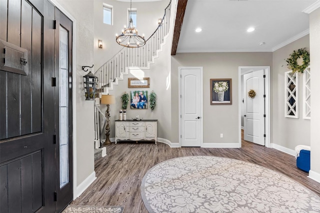 foyer entrance featuring baseboards, a chandelier, stairs, crown molding, and dark wood-type flooring