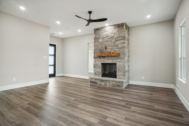 unfurnished living room featuring a stone fireplace, dark wood finished floors, ceiling fan, and a healthy amount of sunlight