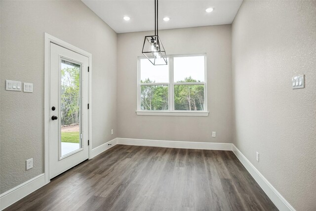 unfurnished dining area featuring a textured wall, baseboards, and dark wood-style flooring