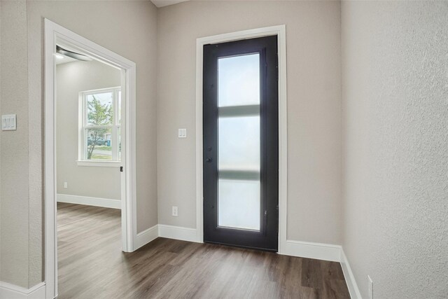 doorway featuring wood finished floors, baseboards, and a textured wall