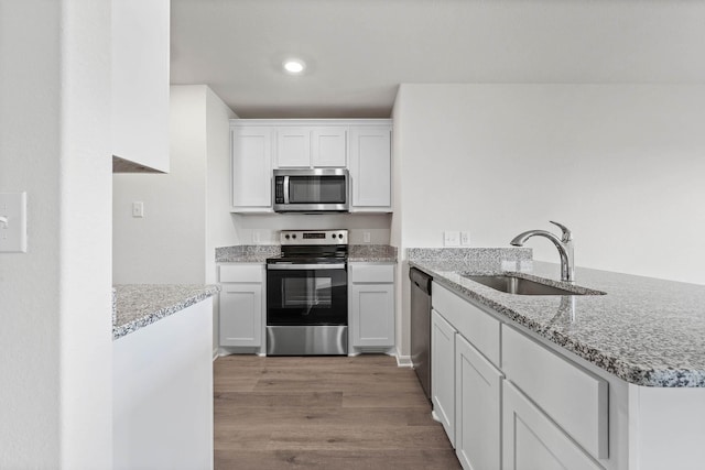 kitchen with a sink, light stone countertops, a peninsula, light wood-style flooring, and appliances with stainless steel finishes