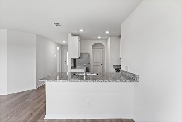 kitchen with white cabinets, arched walkways, freestanding refrigerator, visible vents, and light stone counters