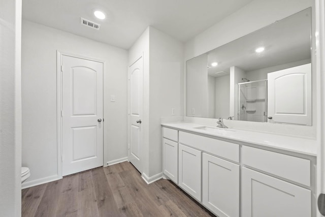 bathroom featuring a shower with shower door, wood finished floors, visible vents, toilet, and vanity