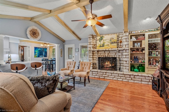living area featuring lofted ceiling with beams, a textured ceiling, a ceiling fan, wood finished floors, and a fireplace