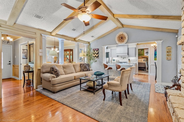 living room with ceiling fan, light wood-style flooring, a textured ceiling, and decorative columns