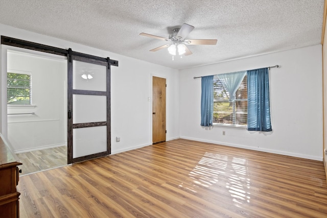 314 Cedar, Mount Pleasant, TX 75455 - spare room with a barn door, wood finished floors, a ceiling fan, baseboards, and a textured ceiling