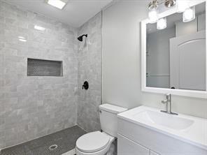 bathroom featuring a tile shower, vanity, and toilet