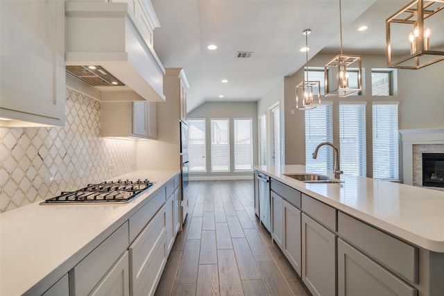 kitchen featuring stainless steel appliances, light countertops, a sink, decorative backsplash, and custom exhaust hood