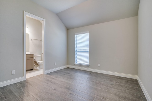 unfurnished bedroom with wood finished floors, lofted ceiling, and baseboards