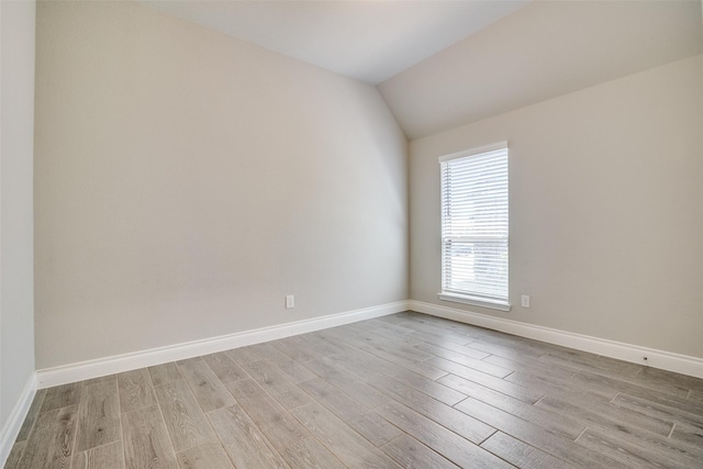 empty room with light wood-type flooring, baseboards, and lofted ceiling