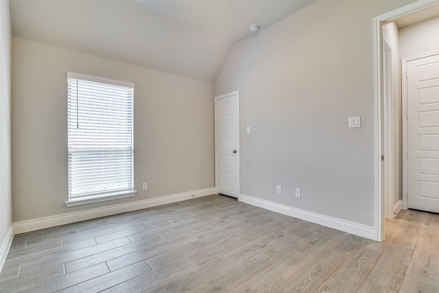 unfurnished room featuring lofted ceiling, a healthy amount of sunlight, light wood finished floors, and baseboards