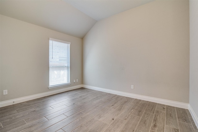 empty room featuring lofted ceiling, light wood-style flooring, and baseboards