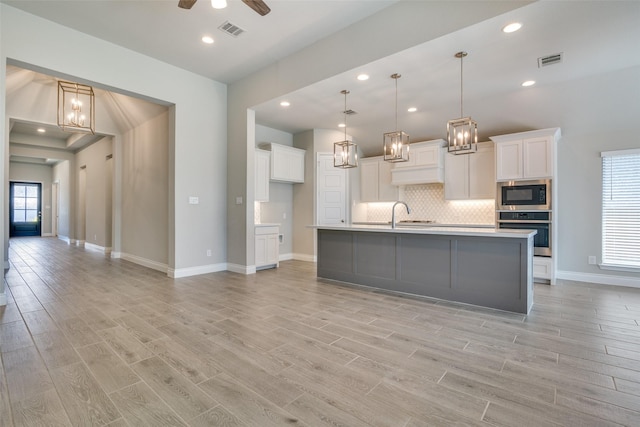 kitchen featuring oven, visible vents, built in microwave, and light wood-type flooring