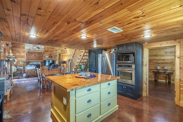 kitchen with wooden walls, visible vents, a kitchen island, concrete floors, and appliances with stainless steel finishes