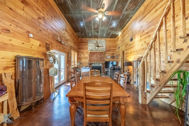 dining room with a ceiling fan, wooden walls, finished concrete floors, and a stone fireplace