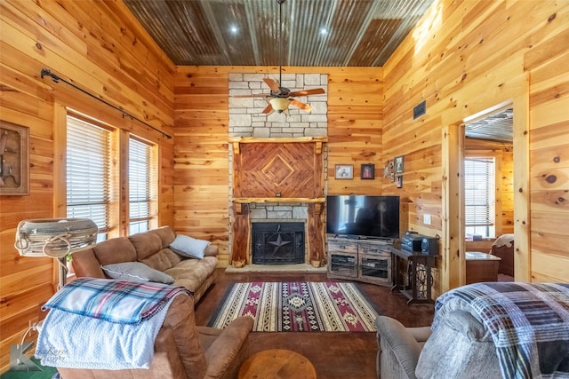 living area with wooden walls, a stone fireplace, wood finished floors, a ceiling fan, and wooden ceiling