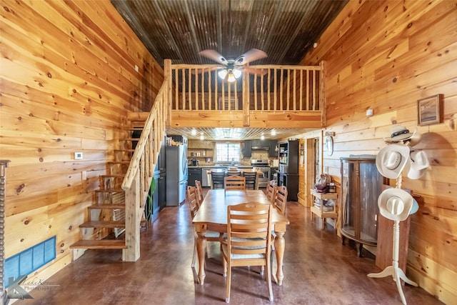 dining space featuring concrete flooring, a ceiling fan, stairs, and wooden walls