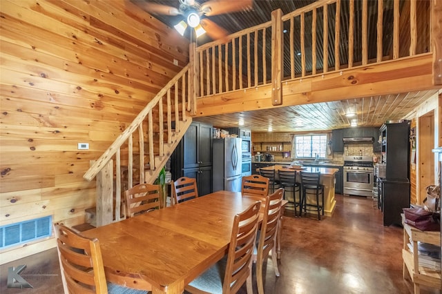 dining space featuring stairs, concrete flooring, wooden walls, ceiling fan, and visible vents