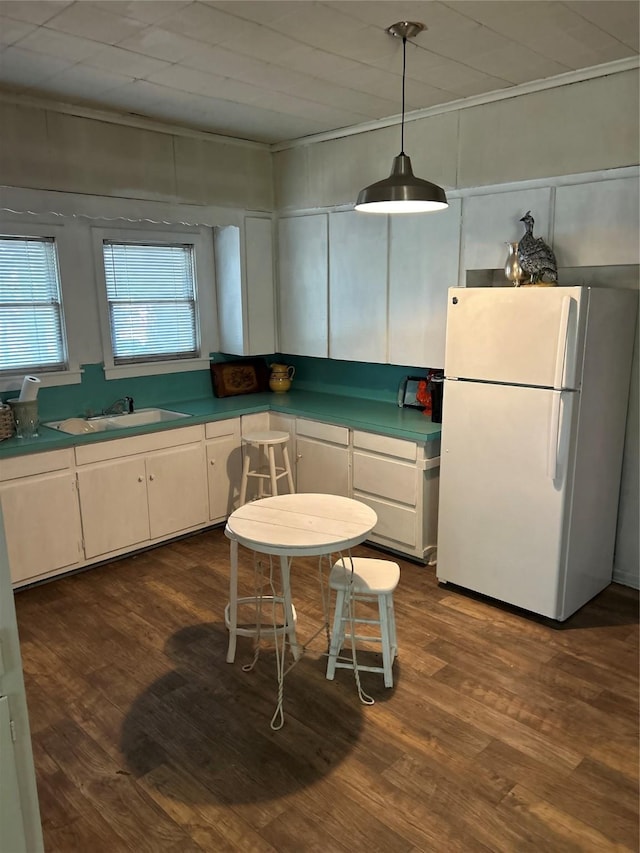kitchen featuring white cabinets, a sink, dark wood-type flooring, freestanding refrigerator, and decorative light fixtures