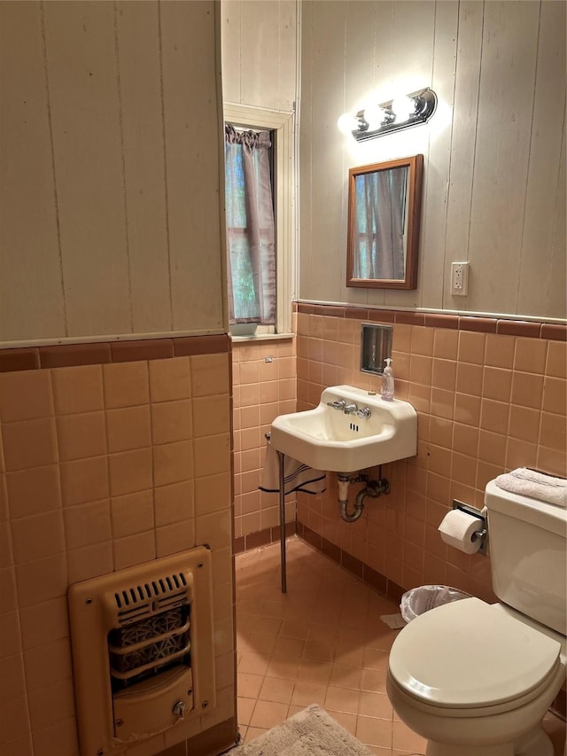 bathroom featuring tile patterned floors, heating unit, toilet, a sink, and tile walls