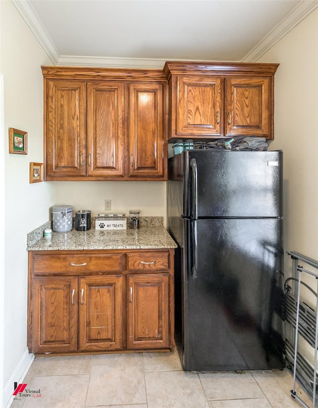 kitchen with brown cabinetry, ornamental molding, light stone counters, and freestanding refrigerator