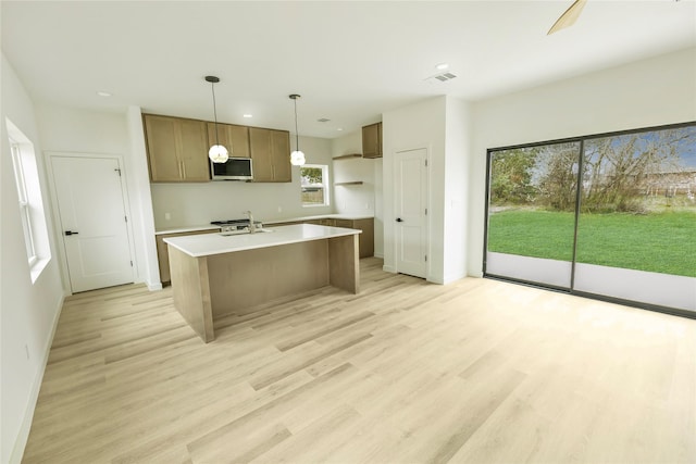 kitchen with light countertops, a sink, stainless steel microwave, light wood-type flooring, and pendant lighting