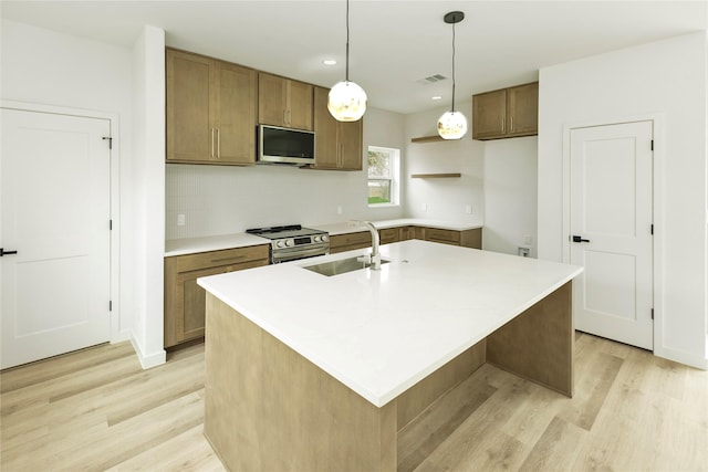 kitchen featuring light wood-type flooring, stainless steel appliances, a sink, and an island with sink